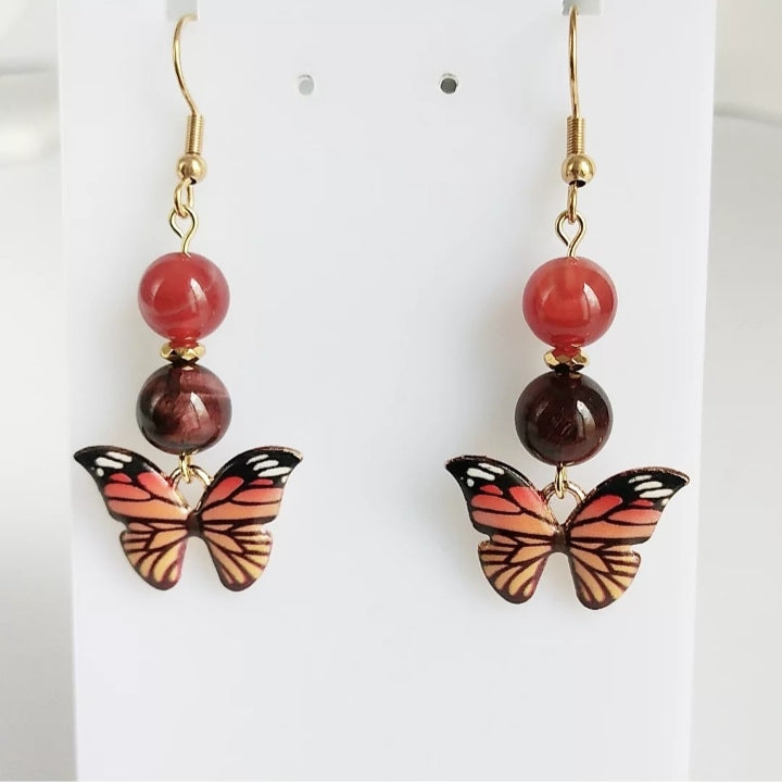 Boucles d'oreilles en pierres naturelles Cornaline & Œil de Taureau avec pendentif papillon – énergie, protection et ancrage. Un bijou spirituel pour vitalité, confiance et équilibre.