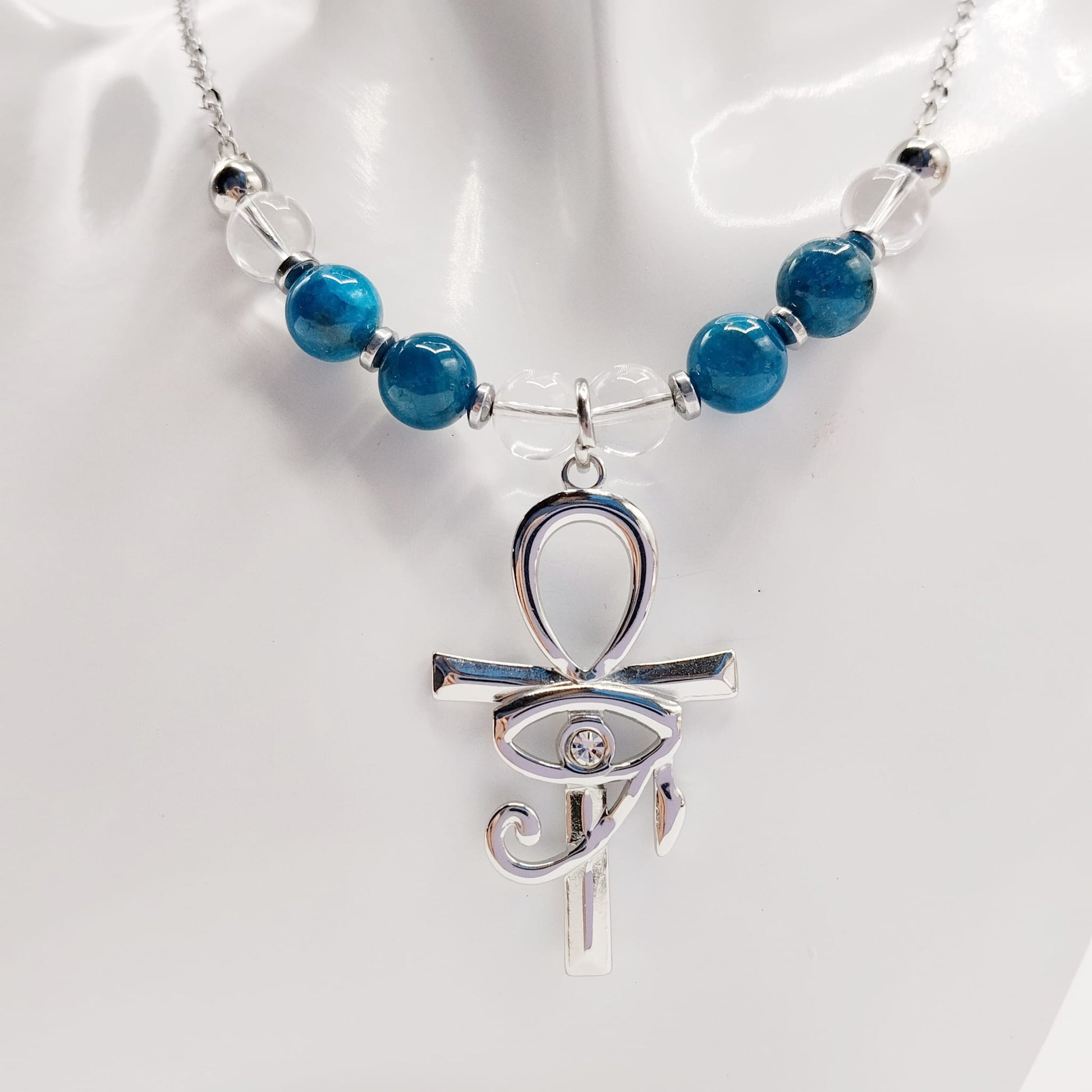 Collier en Apatite et Cristal de Roche avec pendentif Ankh et Œil d’Horus en acier inoxydable. Bijou spirituel favorisant communication, protection et harmonie énergétique.