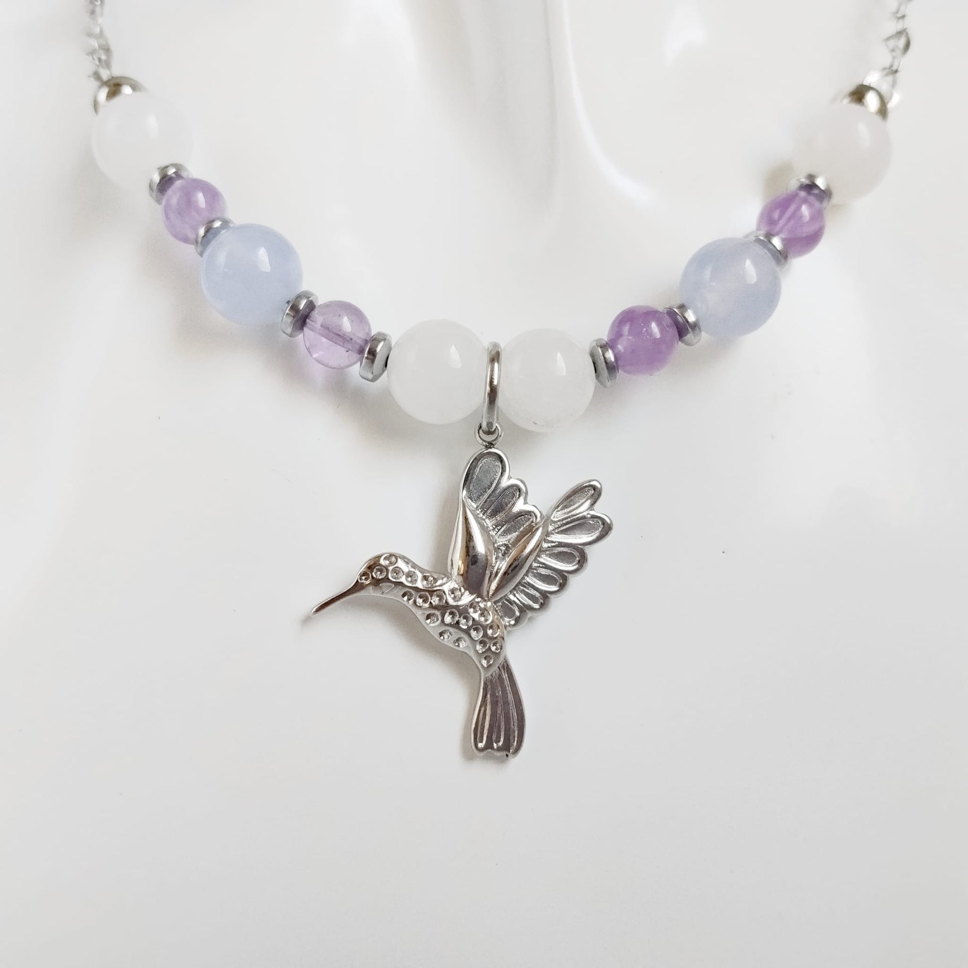 Découvrez notre collier Colibri en Jade blanc, Calcédoine et Améthyste. Un bijou artisanal en pierres naturelles synonyme de sérénité, clarté et douceur.