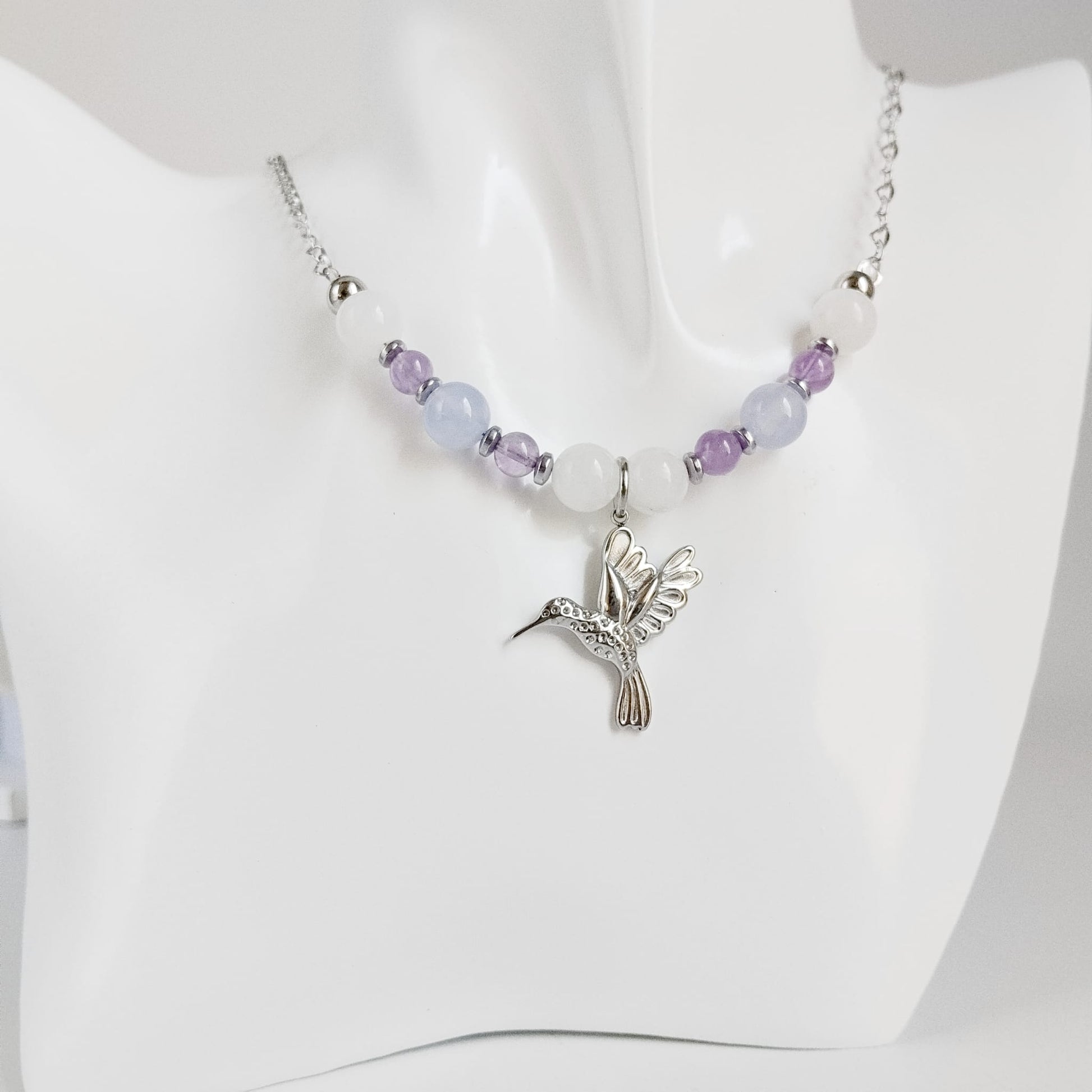 Découvrez notre collier Colibri en Jade blanc, Calcédoine et Améthyste. Un bijou artisanal en pierres naturelles synonyme de sérénité, clarté et douceur.