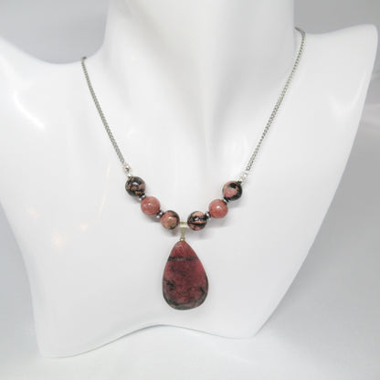 Collier Rhodonite Goutte  https://monjolicaillou.fr/products/collier-rhodonite-goutte  Portez ce bijou avec assurance au quotidien ou lors d'occasions spéciales, et laissez-vous transporter par l'éclat subtil et la sérénité que seule la Rhodonite peut offrir. Avec son mariage parfait entre qualité, style et bien-être, ce collier est bien plus qu'un simple accessoire : c'est une invitation à rayonner 